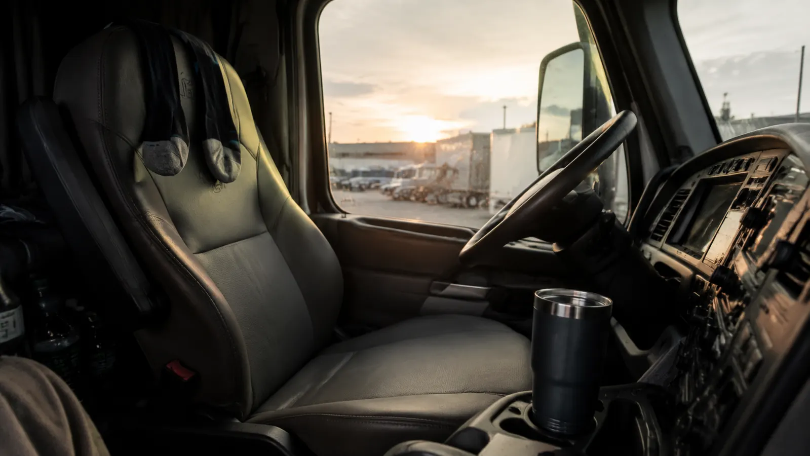 Trucker's boots and lower legs resting on the cab floor after a long day, highway visible through the windshield